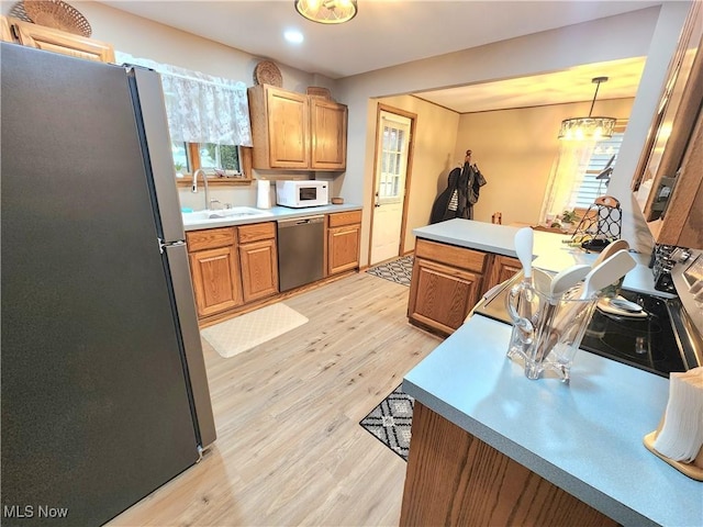 kitchen featuring sink, decorative light fixtures, light wood-type flooring, appliances with stainless steel finishes, and kitchen peninsula