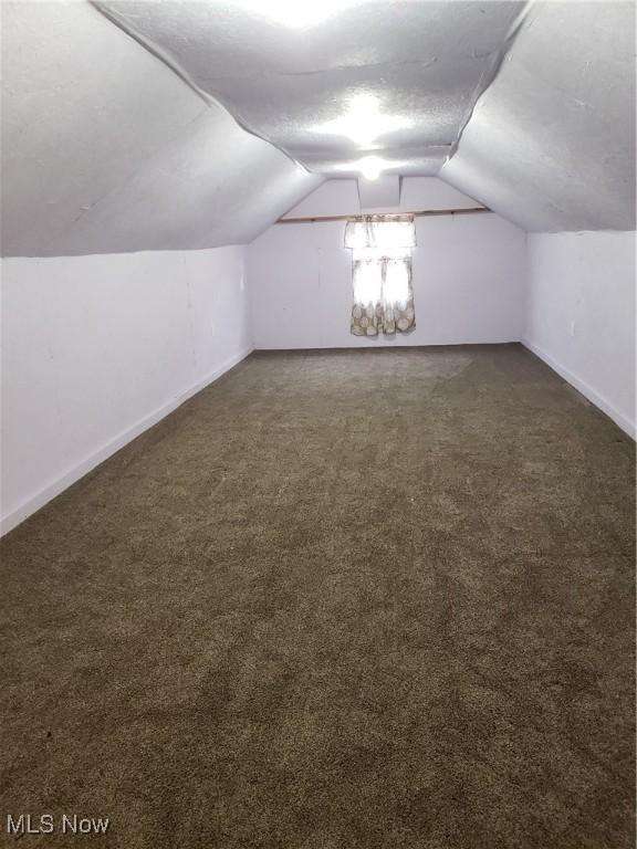 additional living space with lofted ceiling, dark carpet, and a textured ceiling