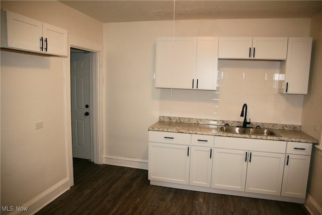 kitchen with dark hardwood / wood-style flooring, light stone countertops, sink, and white cabinets