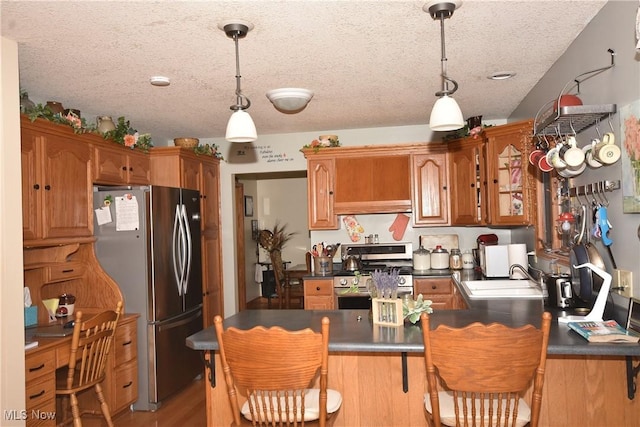 kitchen with sink, appliances with stainless steel finishes, a kitchen bar, decorative light fixtures, and kitchen peninsula