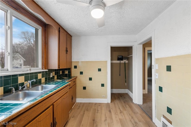 kitchen featuring tile countertops, sink, ceiling fan, a textured ceiling, and light wood-type flooring