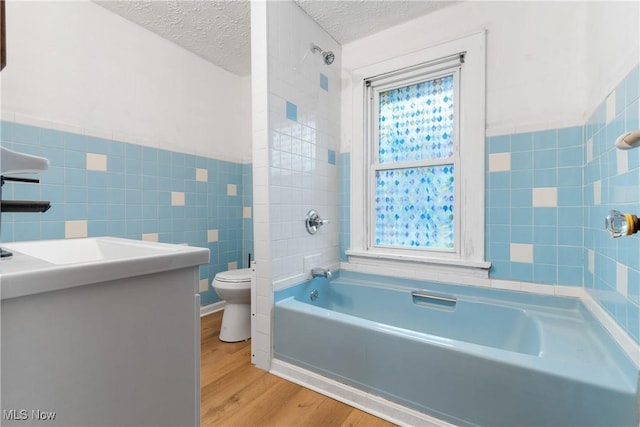 full bathroom with a wealth of natural light, wood-type flooring, tile walls, toilet, and a textured ceiling