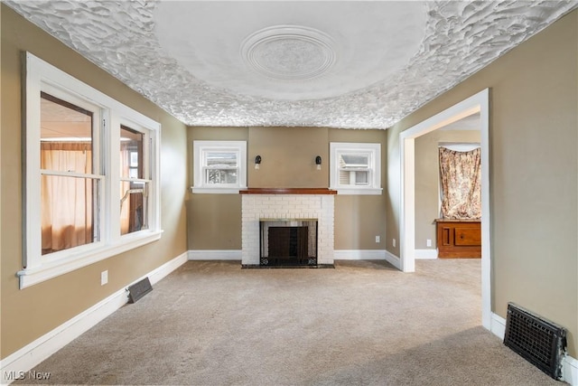 unfurnished living room with a tray ceiling, a brick fireplace, light carpet, and a textured ceiling