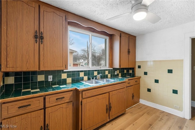 kitchen featuring tile countertops, sink, ceiling fan, light hardwood / wood-style floors, and a textured ceiling