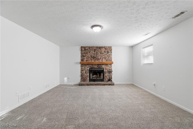 unfurnished living room featuring a stone fireplace, carpet floors, and a textured ceiling