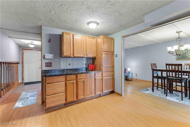 kitchen featuring an inviting chandelier, backsplash, decorative light fixtures, and light wood-type flooring