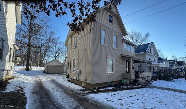 view of snowy exterior featuring a garage, an outdoor structure, and a porch