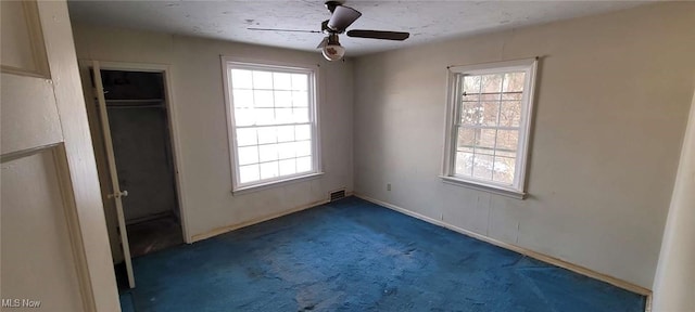 unfurnished bedroom featuring ceiling fan, multiple windows, and dark colored carpet