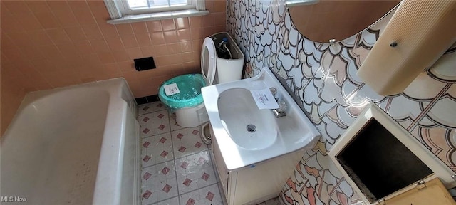 bathroom with tile walls, a bath, sink, and toilet