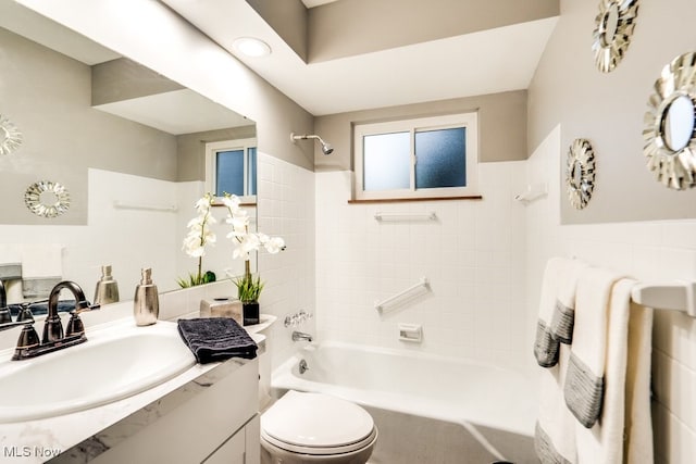 full bathroom featuring tiled shower / bath, vanity, toilet, and tile walls