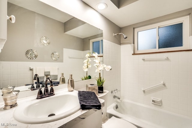 full bathroom featuring toilet, tiled shower / bath combo, sink, and tile walls