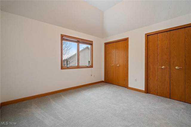 unfurnished bedroom featuring multiple closets, lofted ceiling, and light carpet