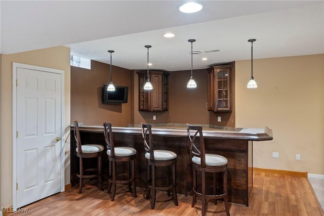 bar with dark brown cabinetry, pendant lighting, and light hardwood / wood-style floors