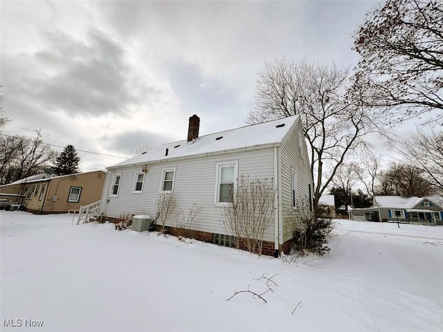 snow covered back of property featuring central AC unit