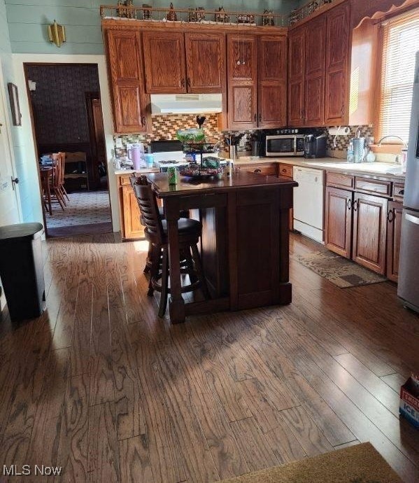 kitchen with dishwasher, dark hardwood / wood-style floors, a kitchen bar, and decorative backsplash