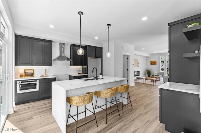 kitchen featuring sink, wall chimney range hood, light stone counters, and wall oven