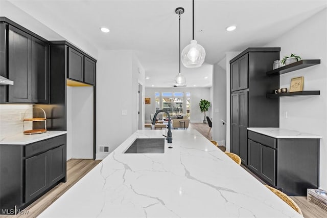 kitchen featuring sink, tasteful backsplash, light stone countertops, light hardwood / wood-style floors, and decorative light fixtures