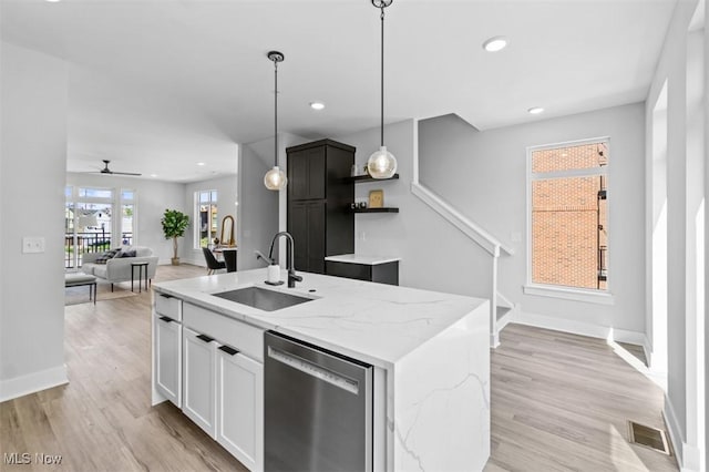 kitchen featuring pendant lighting, dishwasher, white cabinetry, light stone counters, and a center island with sink