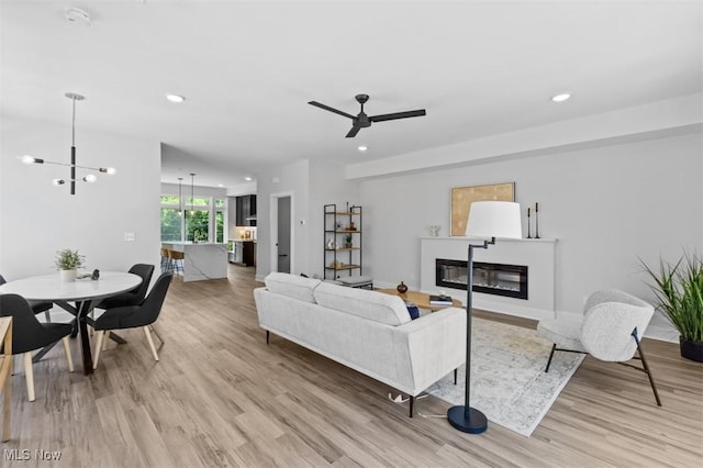 living room with ceiling fan with notable chandelier and light wood-type flooring