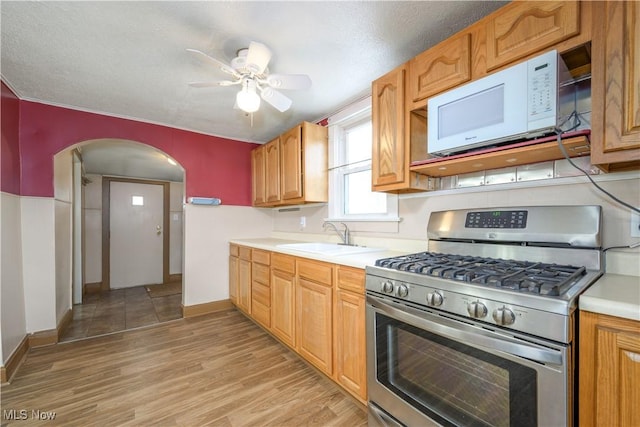 kitchen with sink, ceiling fan, stainless steel gas range, a textured ceiling, and light hardwood / wood-style flooring