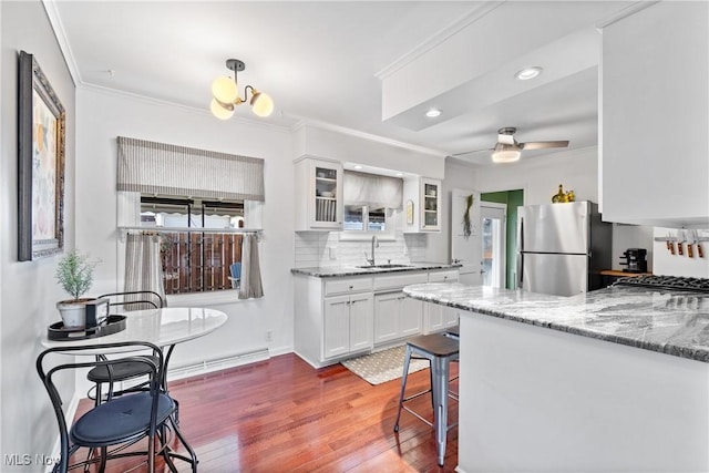 kitchen featuring sink, a breakfast bar area, white cabinetry, crown molding, and stainless steel refrigerator