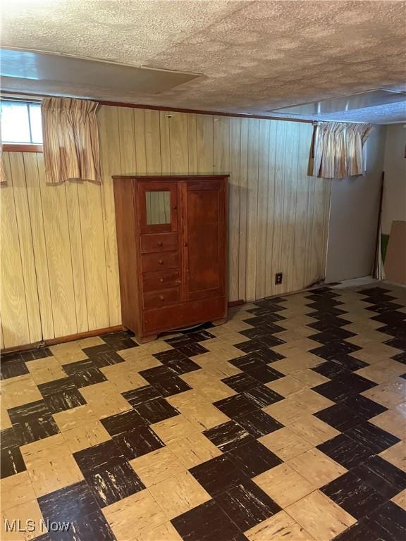 basement featuring wooden walls and a textured ceiling