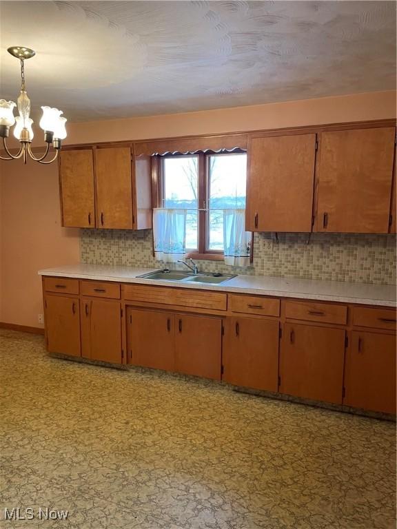 kitchen featuring pendant lighting, an inviting chandelier, sink, and backsplash