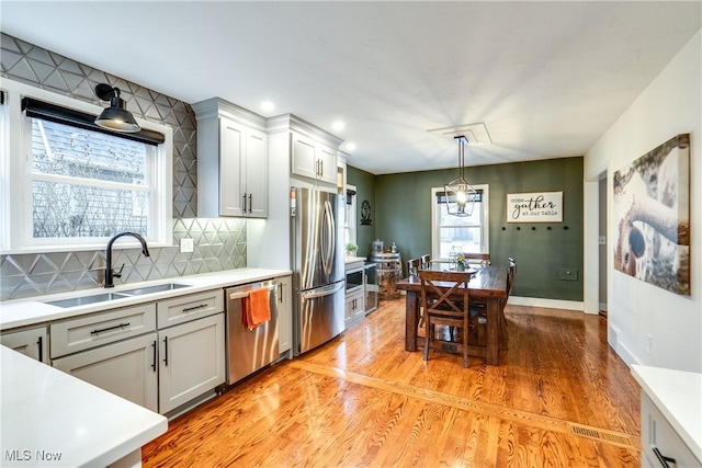 kitchen with sink, appliances with stainless steel finishes, pendant lighting, light hardwood / wood-style floors, and decorative backsplash