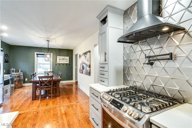 kitchen featuring pendant lighting, stainless steel stove, light hardwood / wood-style flooring, ventilation hood, and decorative backsplash