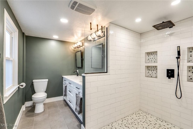 bathroom with tile patterned flooring, vanity, tiled shower, and toilet