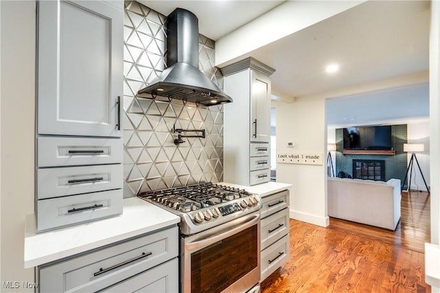 kitchen with decorative backsplash, stainless steel range with gas cooktop, light hardwood / wood-style floors, and wall chimney exhaust hood