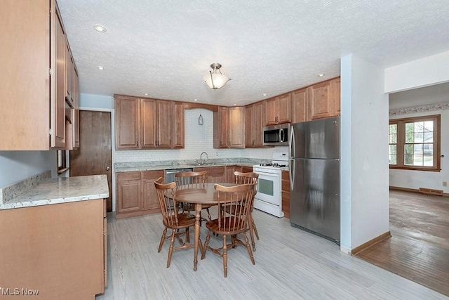 kitchen with sink, appliances with stainless steel finishes, tasteful backsplash, light hardwood / wood-style floors, and a textured ceiling