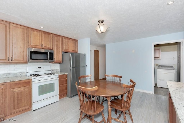 kitchen featuring appliances with stainless steel finishes, washer / dryer, decorative backsplash, and light hardwood / wood-style flooring