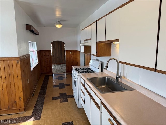 kitchen with wood walls, sink, white gas stove, and white cabinets