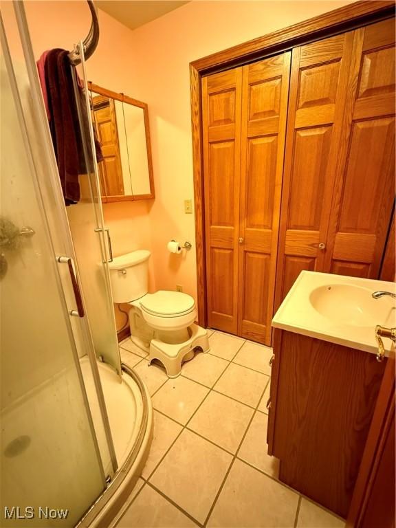 bathroom featuring vanity, a shower with shower door, tile patterned floors, and toilet