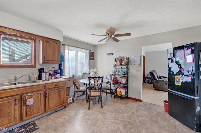 kitchen featuring sink, ceiling fan, a textured ceiling, black fridge, and decorative backsplash