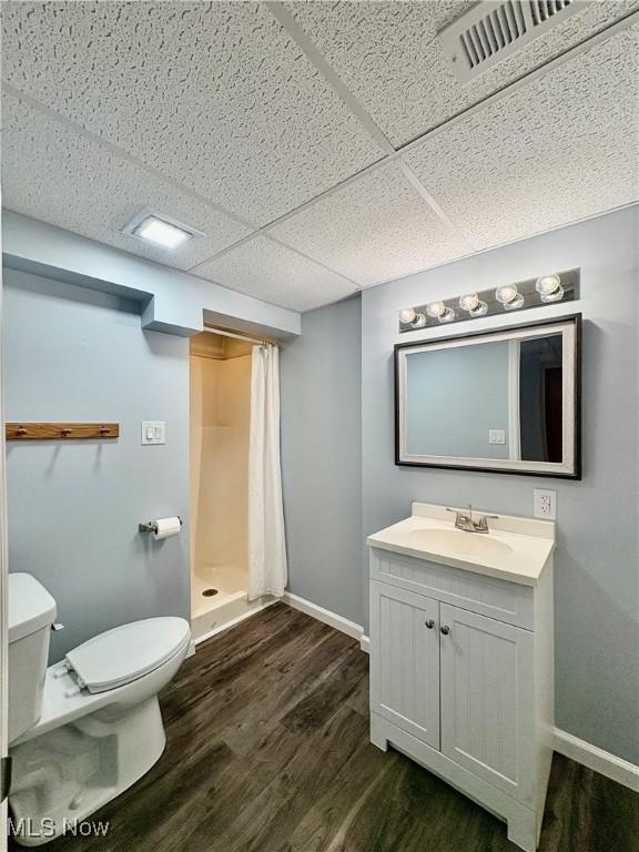 bathroom with a paneled ceiling, hardwood / wood-style floors, vanity, a shower with curtain, and toilet