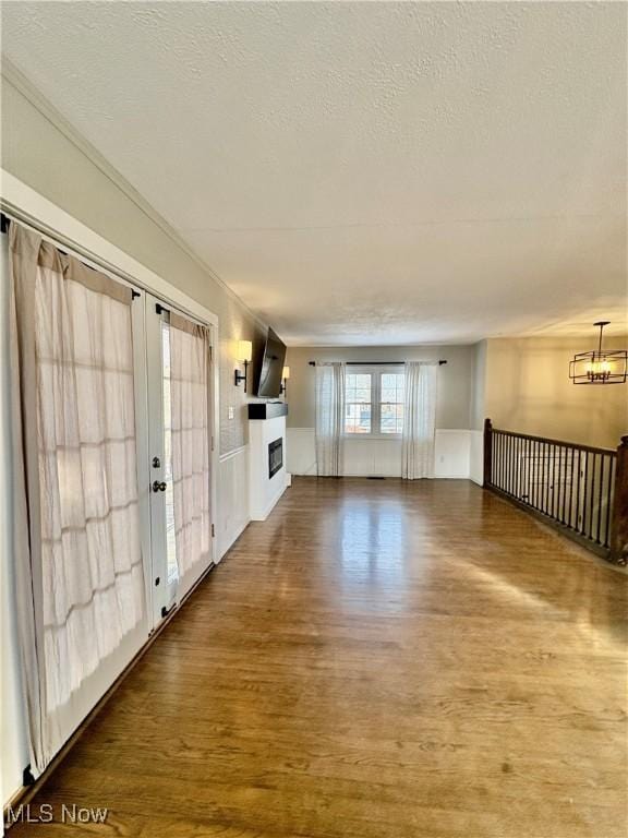 unfurnished living room featuring a notable chandelier, dark wood-type flooring, and a textured ceiling