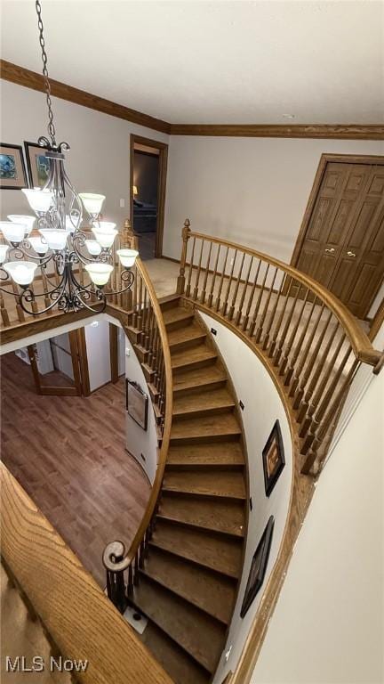 stairway featuring crown molding, hardwood / wood-style flooring, and an inviting chandelier