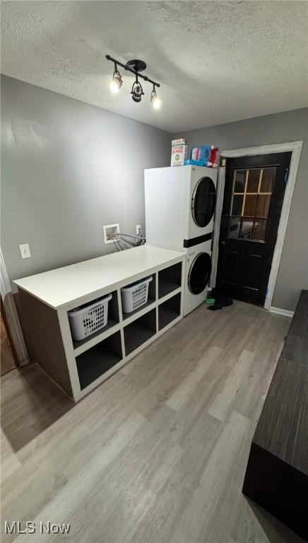 laundry room featuring stacked washer / drying machine, a textured ceiling, and light wood-type flooring