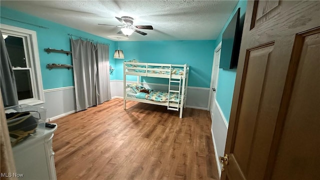 bedroom with ceiling fan, wood-type flooring, and a textured ceiling