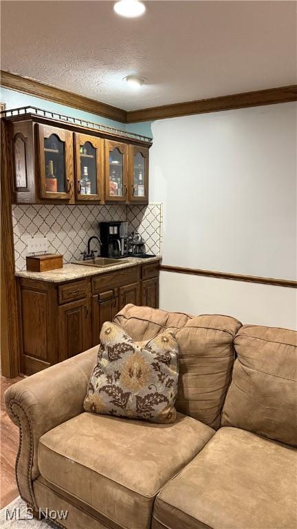 bar featuring sink, crown molding, tasteful backsplash, dark brown cabinetry, and wood-type flooring