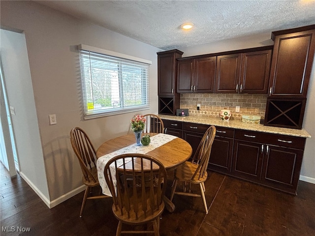 kitchen with dark wood-type flooring, dark brown cabinetry, light stone countertops, and decorative backsplash