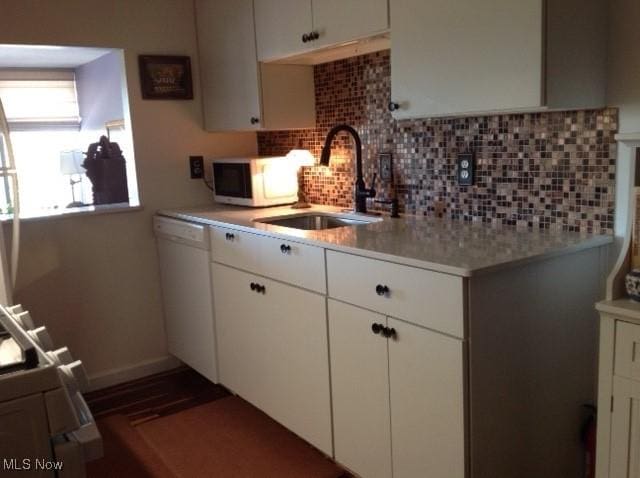 kitchen with white dishwasher, sink, tasteful backsplash, and white cabinets