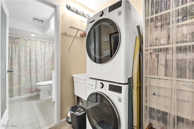 laundry area with stacked washer and clothes dryer and light tile patterned floors