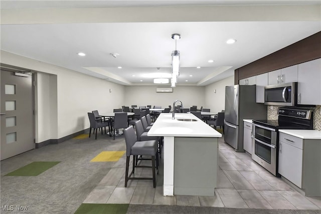 kitchen with sink, appliances with stainless steel finishes, backsplash, an island with sink, and a kitchen bar