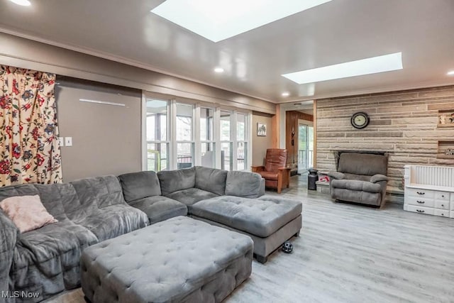 living room featuring crown molding, wood-type flooring, a stone fireplace, and a skylight