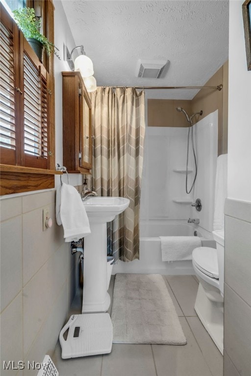 bathroom with shower / bathtub combination with curtain, tile patterned floors, toilet, and a textured ceiling