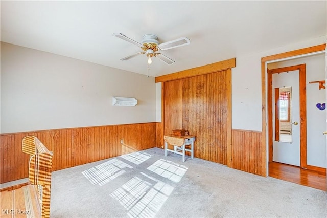 unfurnished room featuring ceiling fan, wooden walls, and light carpet