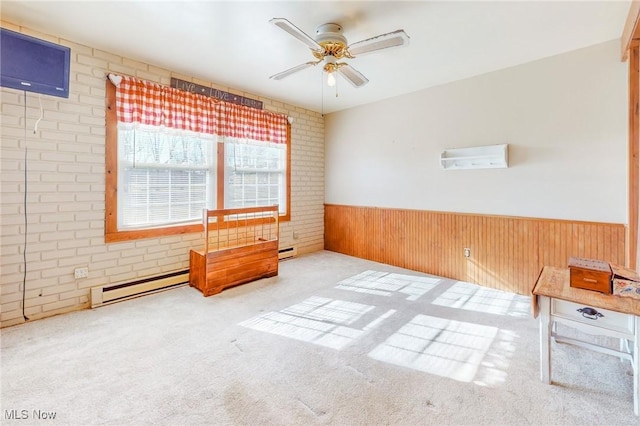 carpeted empty room featuring a baseboard radiator, brick wall, wooden walls, and ceiling fan